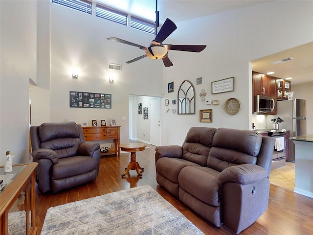 living room with light hardwood / wood-style floors, ceiling fan, and a towering ceiling