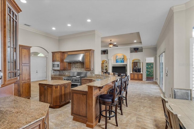 kitchen featuring arched walkways, brown cabinets, stainless steel appliances, visible vents, and wall chimney exhaust hood