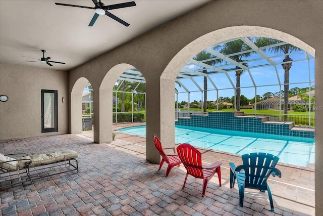 outdoor pool with glass enclosure, a patio area, and a ceiling fan