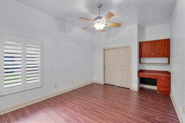 unfurnished bedroom featuring dark wood-style floors, a closet, baseboards, and built in desk