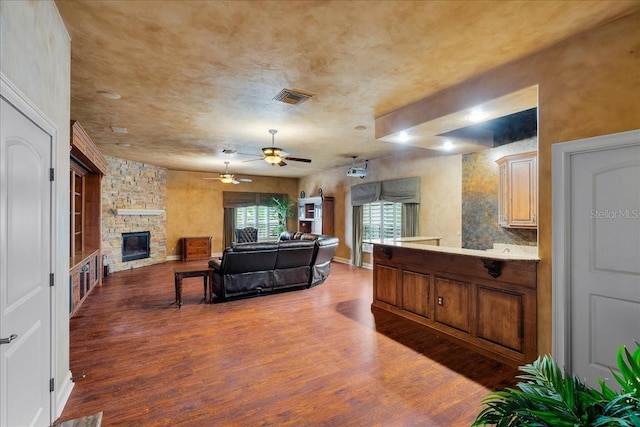 living room with ceiling fan, a stone fireplace, wood finished floors, and visible vents