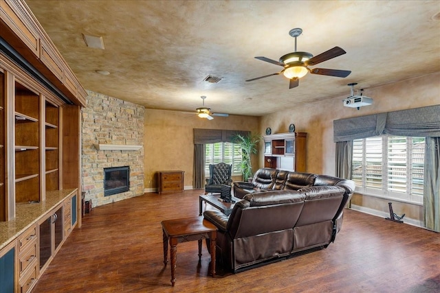 living room featuring a stone fireplace, dark wood finished floors, visible vents, and a ceiling fan