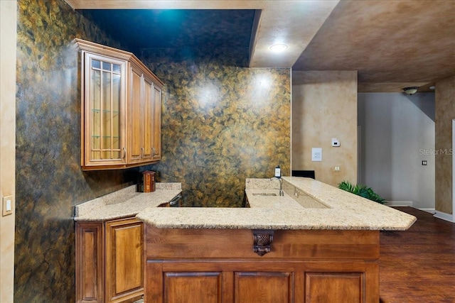 kitchen with dark wood finished floors, light stone counters, brown cabinets, glass insert cabinets, and a sink