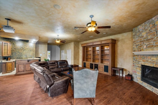 living room with visible vents, ceiling fan, a stone fireplace, and wood finished floors