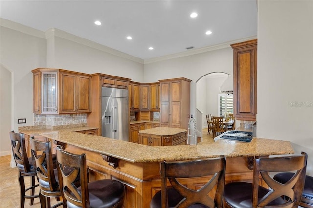 kitchen featuring arched walkways, crown molding, decorative backsplash, a peninsula, and built in refrigerator