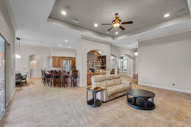 living room featuring arched walkways, baseboards, visible vents, and a tray ceiling