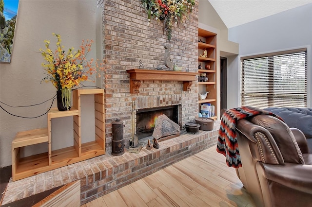 living room with vaulted ceiling, a brick fireplace, built in shelves, a textured ceiling, and wood-type flooring