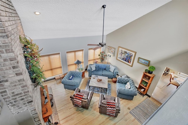 living room with ceiling fan, wood-type flooring, a textured ceiling, and vaulted ceiling