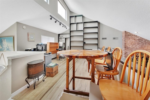 dining room with light wood-type flooring, a textured ceiling, and vaulted ceiling