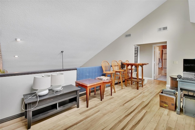 interior space with light hardwood / wood-style floors, a textured ceiling, and high vaulted ceiling