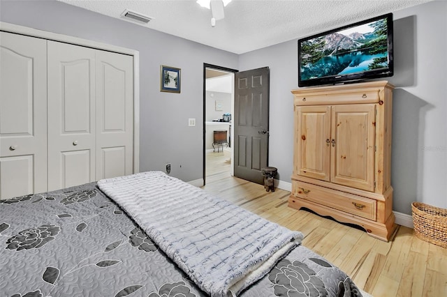 bedroom with a textured ceiling, a closet, light hardwood / wood-style flooring, and ceiling fan