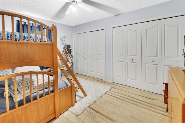 bedroom featuring ceiling fan, light wood-type flooring, a textured ceiling, and multiple closets