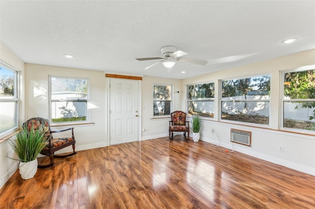 sitting room with a textured ceiling, hardwood / wood-style flooring, an AC wall unit, and ceiling fan