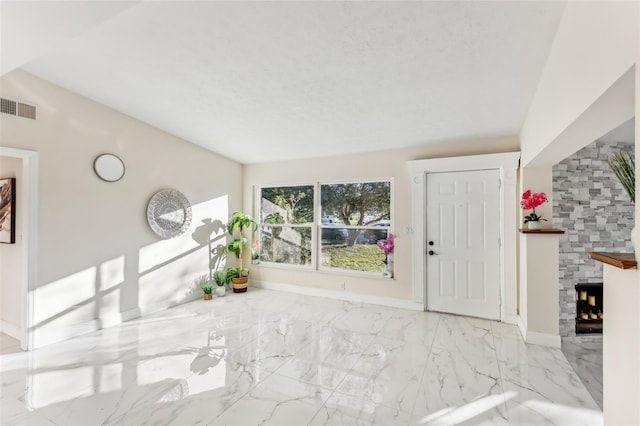 entryway with vaulted ceiling and a stone fireplace