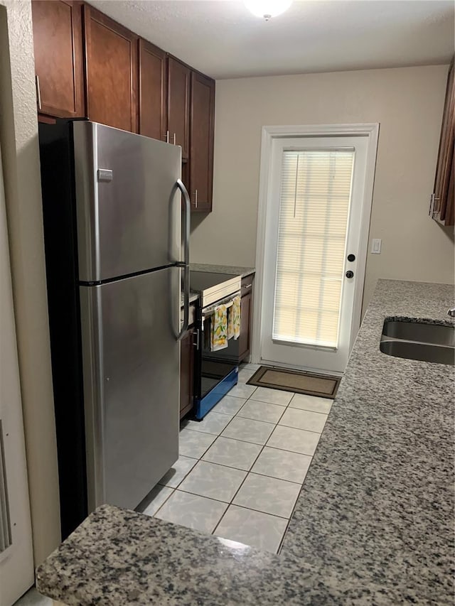 kitchen featuring sink, light tile patterned floors, stainless steel refrigerator, electric range, and light stone countertops