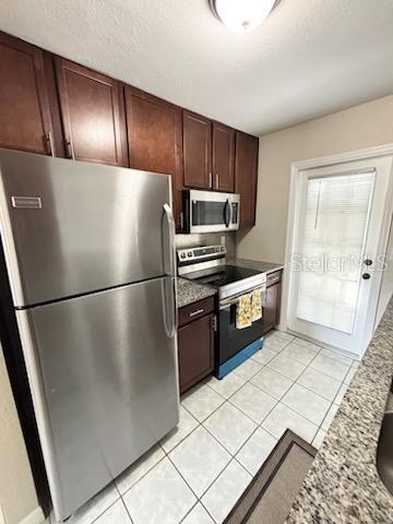 kitchen with light stone counters, light tile patterned flooring, a textured ceiling, and appliances with stainless steel finishes