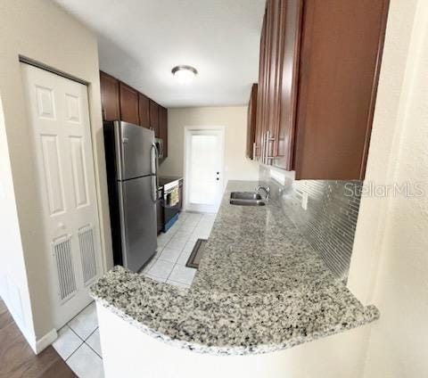 kitchen featuring light tile patterned flooring, stainless steel refrigerator, sink, light stone counters, and kitchen peninsula