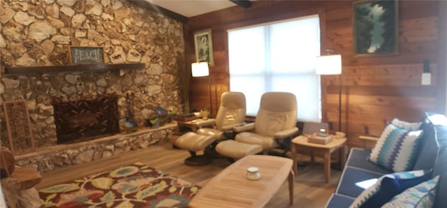 living room with hardwood / wood-style floors, a stone fireplace, and wooden walls