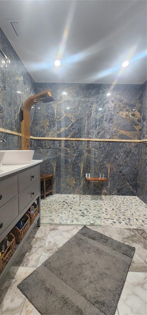 bathroom with a tile shower, vanity, and tile walls