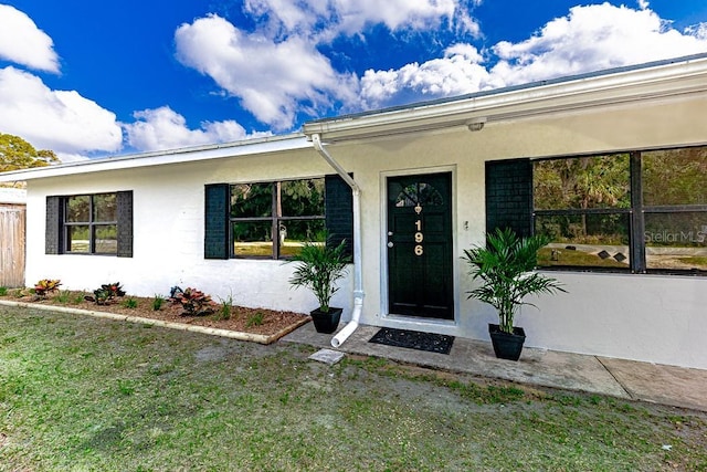 view of exterior entry featuring a lawn and stucco siding