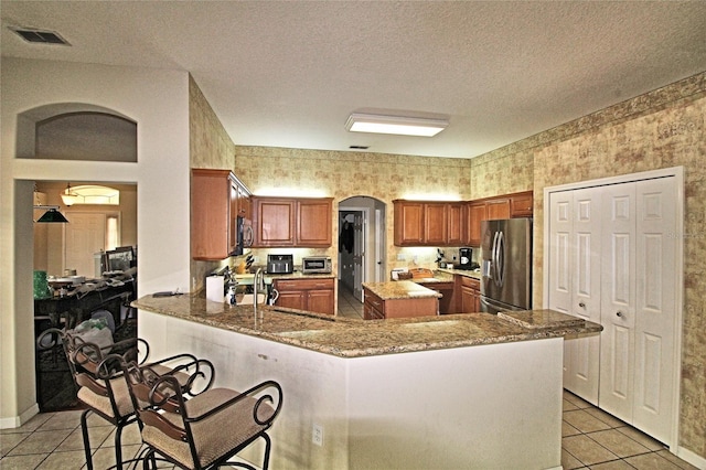 kitchen with stainless steel fridge with ice dispenser, kitchen peninsula, a textured ceiling, a breakfast bar, and light tile patterned floors