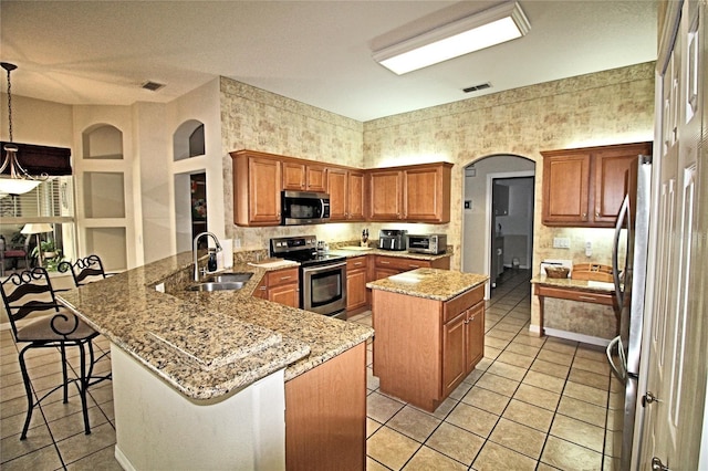 kitchen featuring sink, stainless steel appliances, kitchen peninsula, decorative light fixtures, and a breakfast bar area