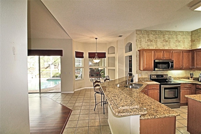 kitchen with kitchen peninsula, appliances with stainless steel finishes, a kitchen breakfast bar, sink, and decorative light fixtures