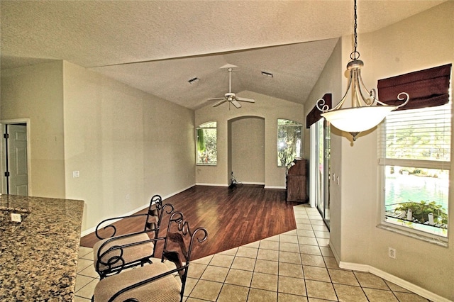 interior space featuring a textured ceiling, ceiling fan, light tile patterned flooring, and lofted ceiling