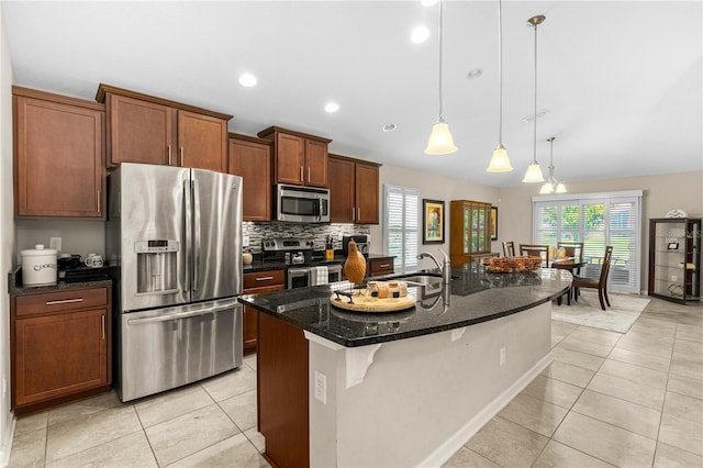 kitchen featuring a kitchen island with sink, sink, light tile patterned floors, appliances with stainless steel finishes, and decorative light fixtures