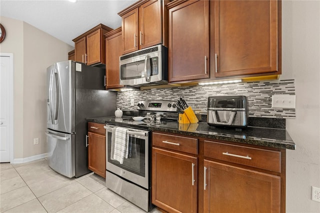 kitchen with appliances with stainless steel finishes, backsplash, light tile patterned floors, and dark stone countertops