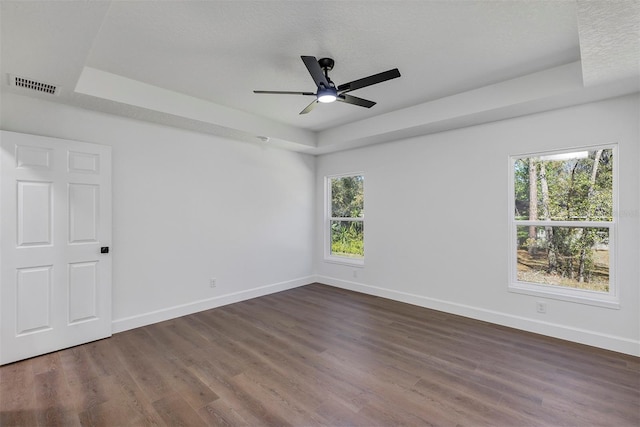 empty room featuring a tray ceiling, dark wood-type flooring, visible vents, and baseboards