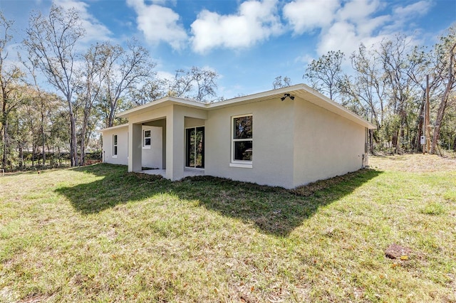 rear view of house featuring a lawn and stucco siding