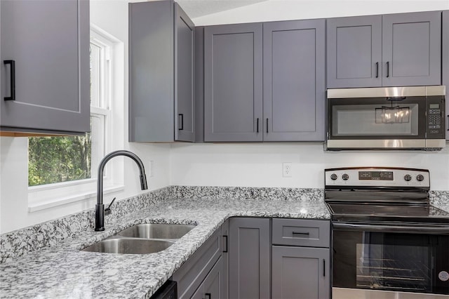 kitchen with lofted ceiling, appliances with stainless steel finishes, a sink, and light stone counters