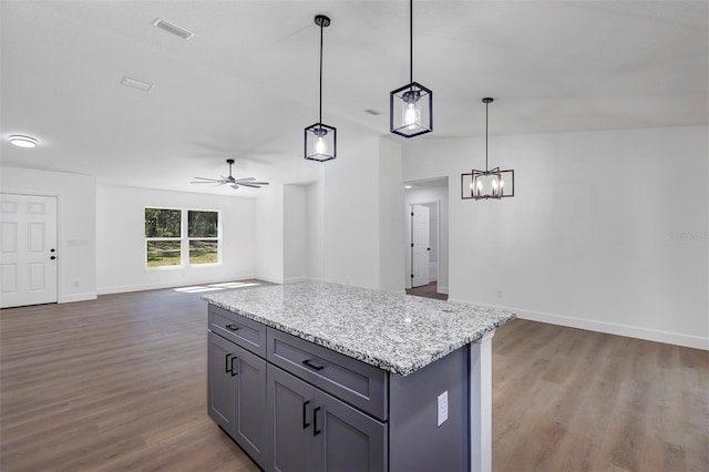 kitchen with visible vents, a kitchen island, light stone counters, open floor plan, and wood finished floors