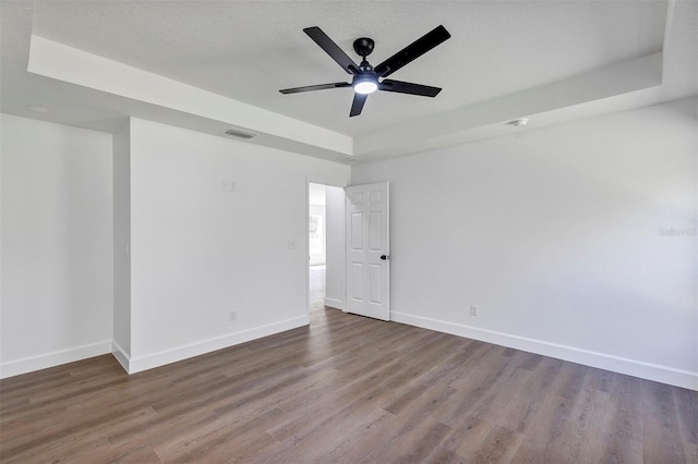 spare room featuring a ceiling fan, baseboards, a tray ceiling, and wood finished floors