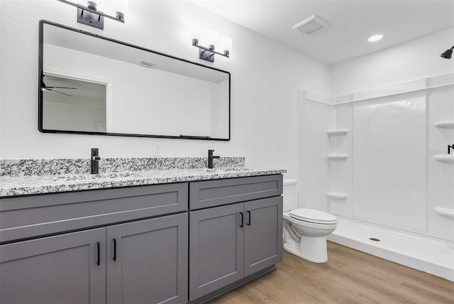 full bathroom with double vanity, toilet, wood finished floors, walk in shower, and a sink