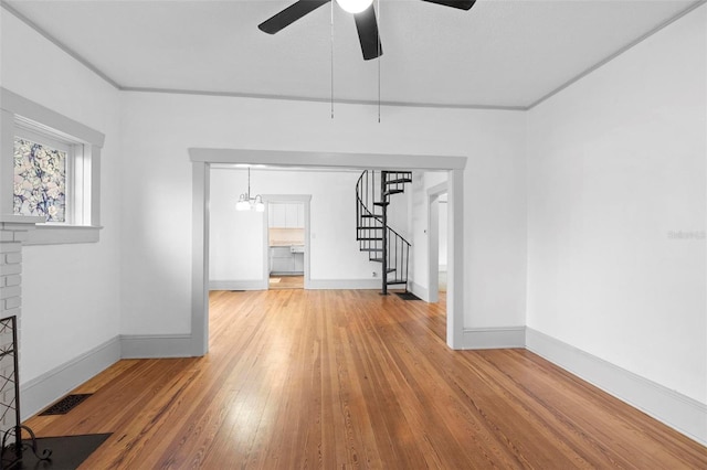 empty room with hardwood / wood-style flooring, ceiling fan with notable chandelier, and a brick fireplace