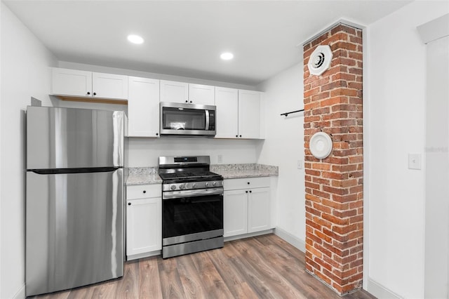 kitchen featuring light stone counters, wood-type flooring, white cabinetry, and stainless steel appliances