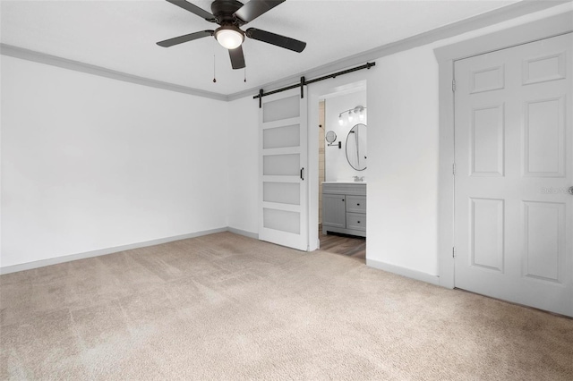 unfurnished bedroom with connected bathroom, ceiling fan, a barn door, light carpet, and ornamental molding