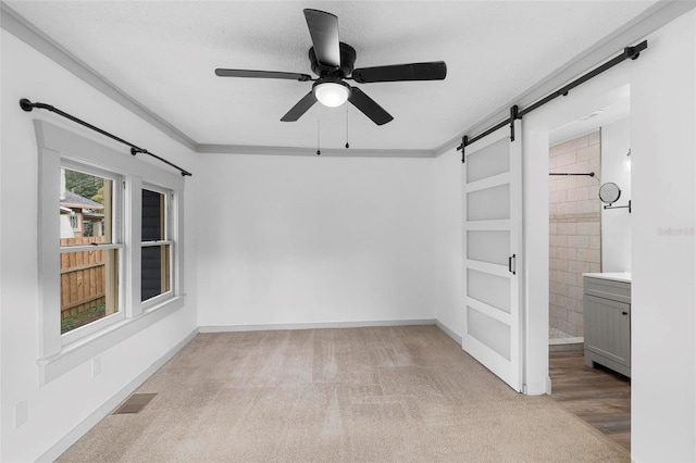 carpeted spare room featuring ceiling fan, a barn door, ornamental molding, and a textured ceiling