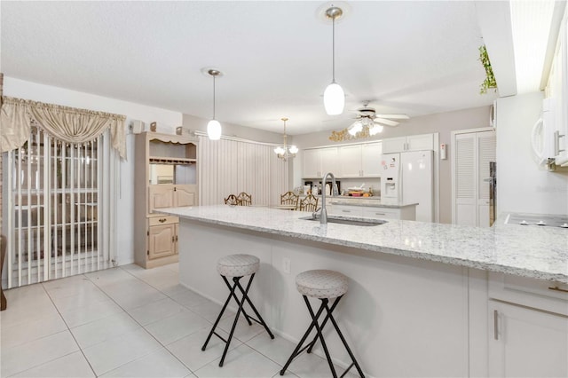 kitchen with white cabinetry, sink, light stone counters, white refrigerator with ice dispenser, and ceiling fan with notable chandelier