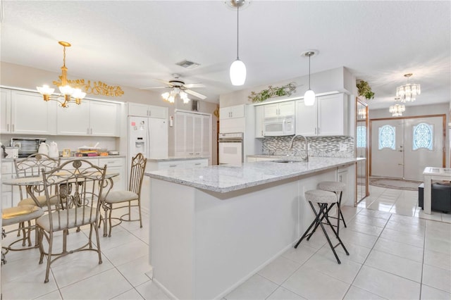 kitchen with white appliances, ceiling fan with notable chandelier, sink, hanging light fixtures, and white cabinetry