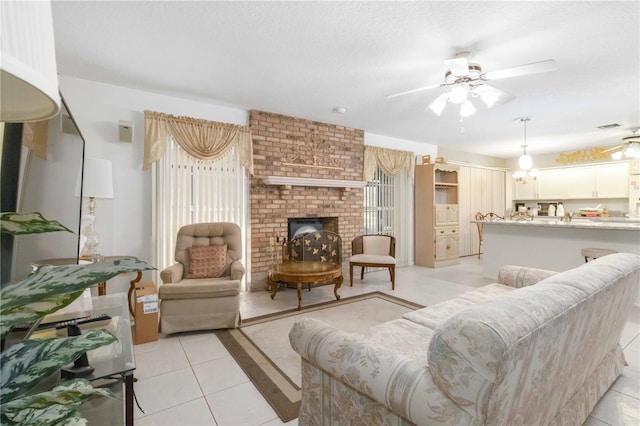 tiled living room featuring ceiling fan, a textured ceiling, and a brick fireplace