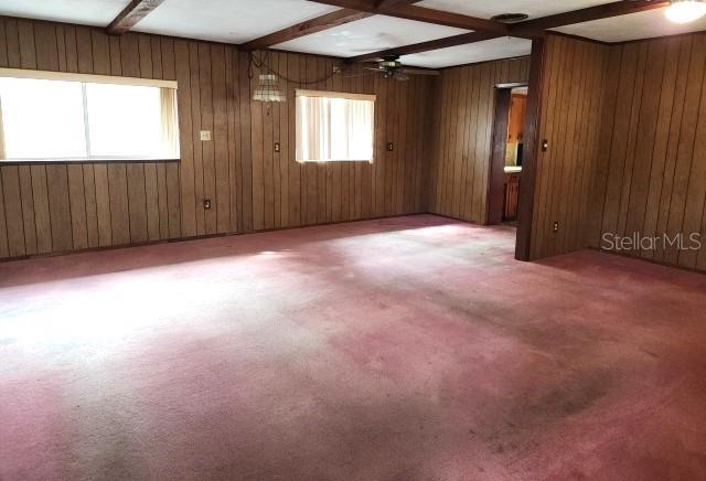 empty room with beam ceiling, ceiling fan, coffered ceiling, wood walls, and carpet floors