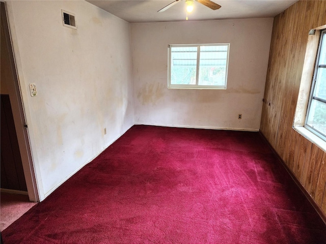 unfurnished room with wood walls, ceiling fan, and dark colored carpet