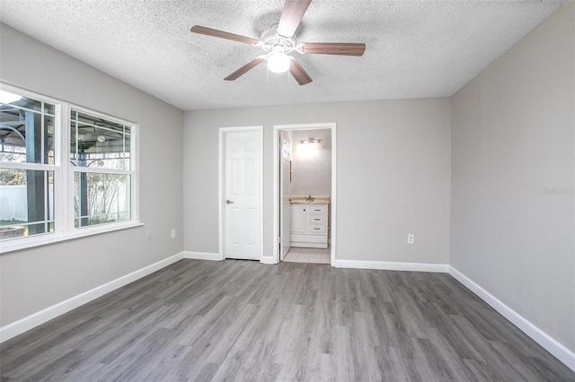 unfurnished bedroom with ceiling fan, ensuite bath, dark hardwood / wood-style floors, and a textured ceiling