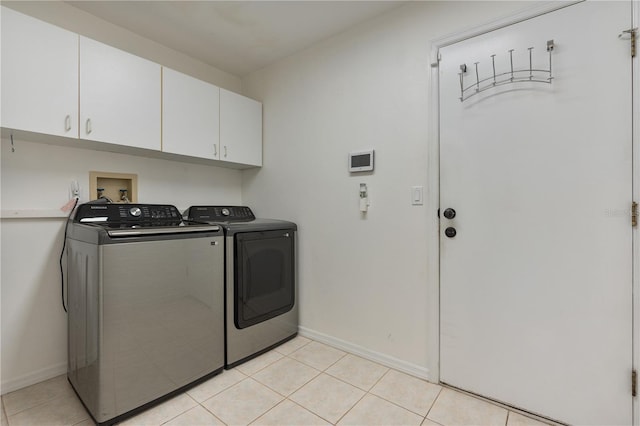 clothes washing area with cabinets, light tile patterned floors, and washing machine and clothes dryer