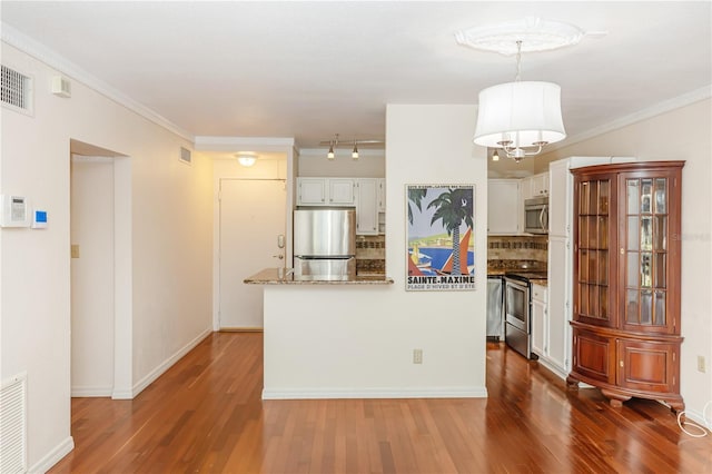 kitchen featuring decorative backsplash, stainless steel appliances, crown molding, decorative light fixtures, and white cabinets