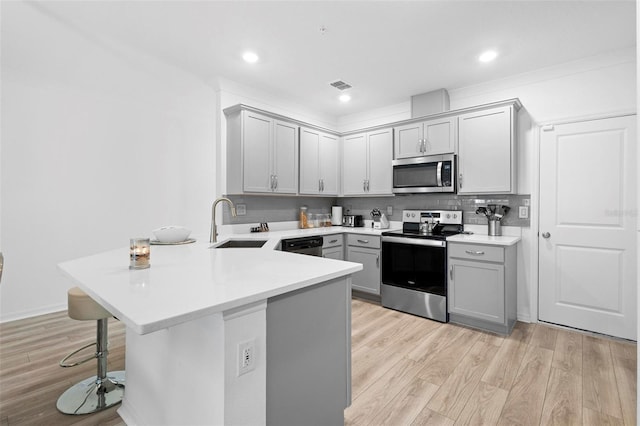 kitchen with gray cabinetry, light hardwood / wood-style flooring, kitchen peninsula, a breakfast bar area, and appliances with stainless steel finishes