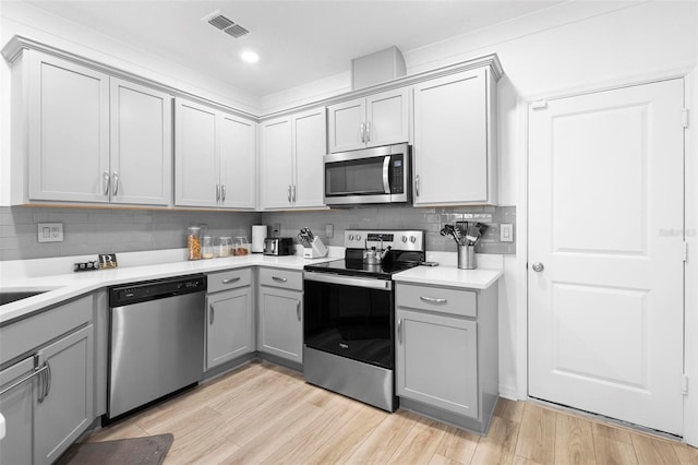 kitchen featuring tasteful backsplash, gray cabinetry, stainless steel appliances, and light wood-type flooring